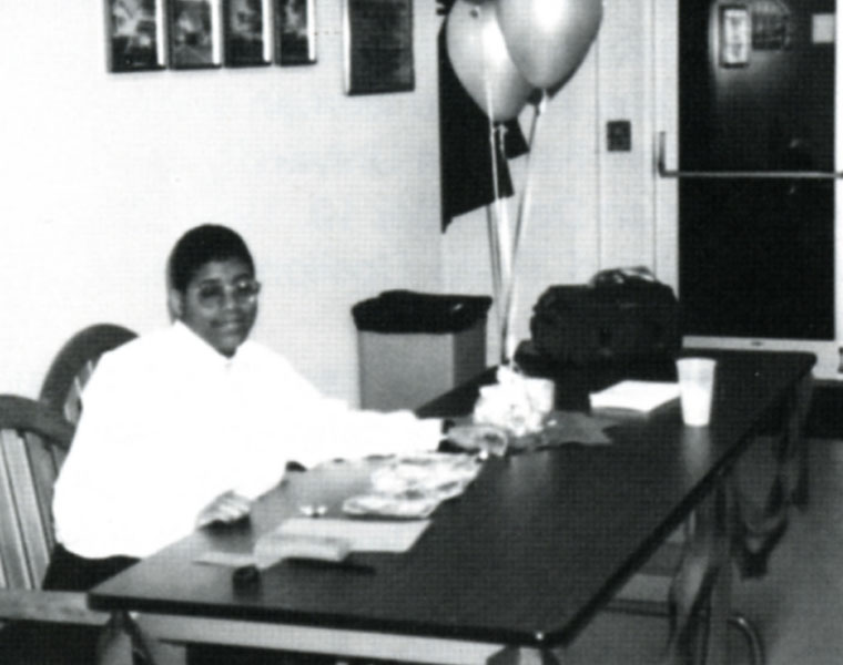 Photo of someone sitting at a desk with balloons in a black and white photo from a Lavender Ball from the 1990s