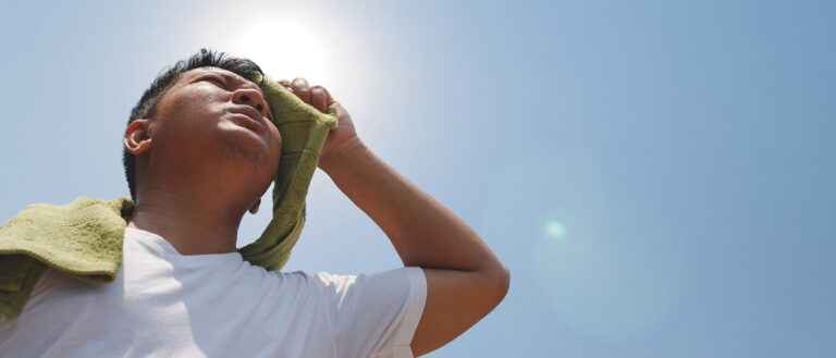 Asian man under a bright sun wiping his face with towler