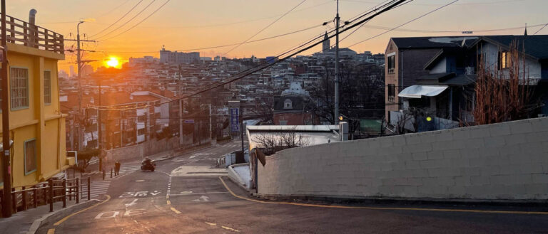 Photo looking down a nearly empty road in Seoul, South Korea, with buildings in the background and the sun setting