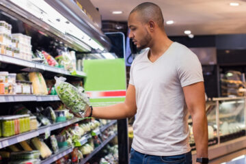 Photo of a man looking at a bag of lettuce while grocery shopping