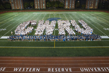 Photo of the Class of 2026 and OLs spelling out the letters C-W-R-U on DiSanto Field