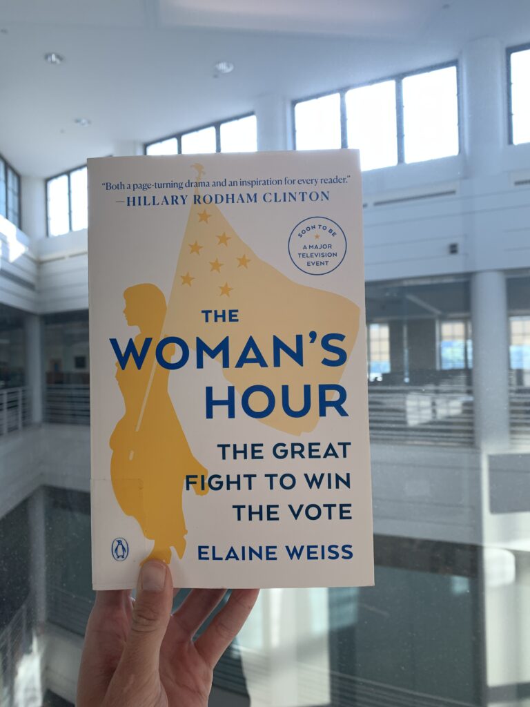 Photo of a hand holding up the book "The Woman's Hour" in Kelvin Smith Library