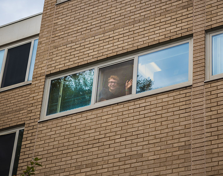 Student waving from through a dorm room window