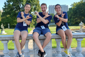 Orientation leaders Michelle Yun, Grant Boone and Gillian Russo pose for a photo at Wade Oval while holding their hands up in an OL shape