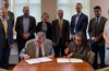photograph of CWRU president Eric Kaler, left, and Lawrence Livermore National Lab Director Kim Budil, right, signing a document, surrounded by a group of officials