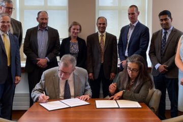 photograph of CWRU president Eric Kaler, left, and Lawrence Livermore National Lab Director Kim Budil, right, signing a document, surrounded by a group of offiicials