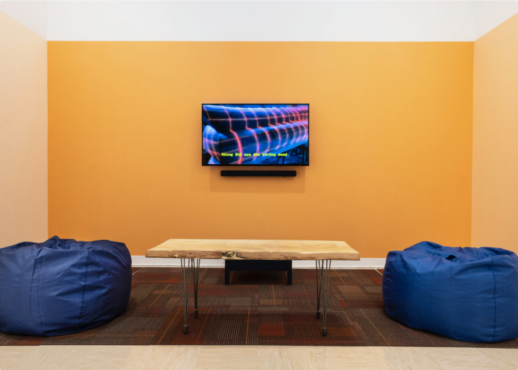Photo of a room with a TV screen on a wall with blue bean bag chairs and bright yellow walls