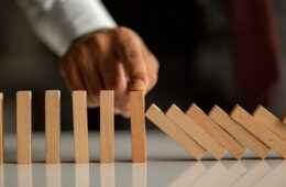 Photo of a man's finger holding up a domino while others fall around it