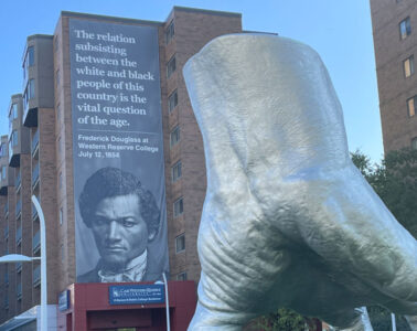 Photo of the Frederick Douglass banner hanging off the University Bookstore that quotes him: “The relation subsisting between the white and black people of this country is the vital question of the age.” with Judy's hand statue in front of it