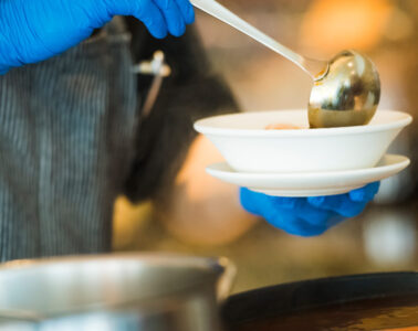 Close up photo of someone holding a ladle and filling a bowl with soup