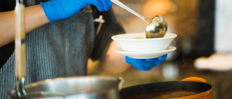 Close up photo of someone holding a ladle and filling a bowl with soup