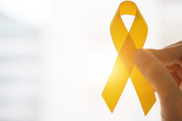 Photo of a hand holding up a yellow suicide prevention ribbon as light shines through representing hope