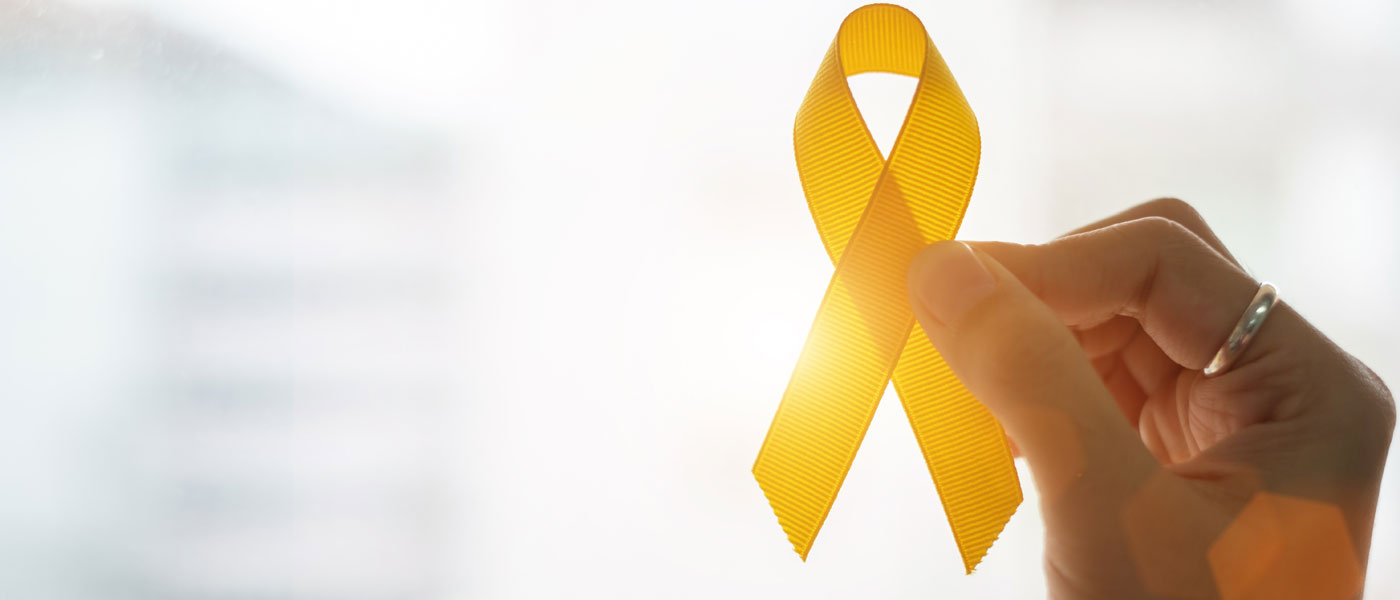 Photo of a hand holding up a yellow suicide prevention ribbon as light shines through representing hope