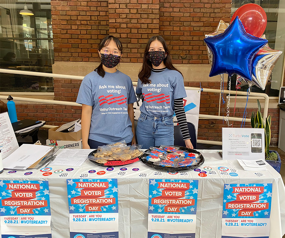 Two voting ambassadors stand at a table with treats on Voter Registration Day in 2021