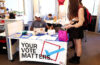 Photo of a student helping others to register to vote at a table with a banner that says "your vote matters"