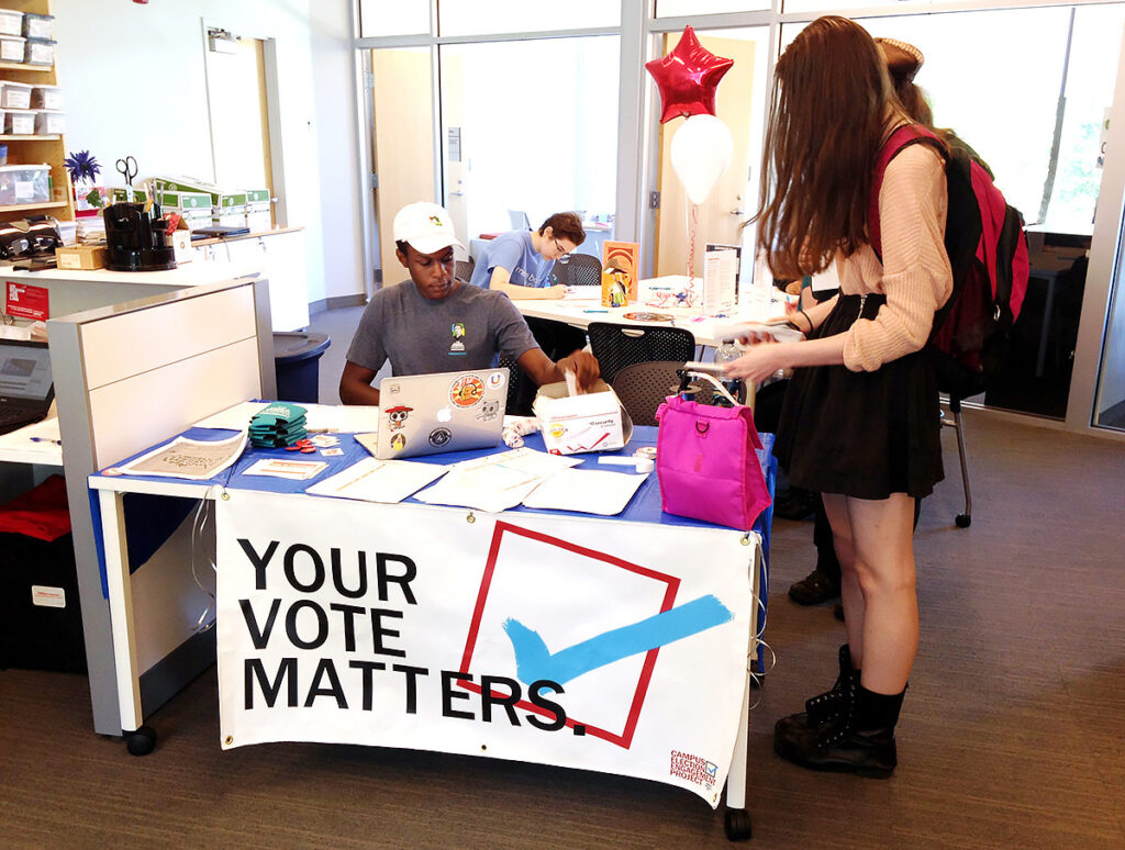 Photo of a student helping others to register to vote at a table with a banner that says "your vote matters"