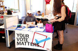 Photo of a student helping others to register to vote at a table with a banner that says "your vote matters"