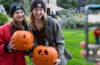 Photo taken from over someone's shoulder showing them taking a photo of two CWRU students holding carved pumpkins