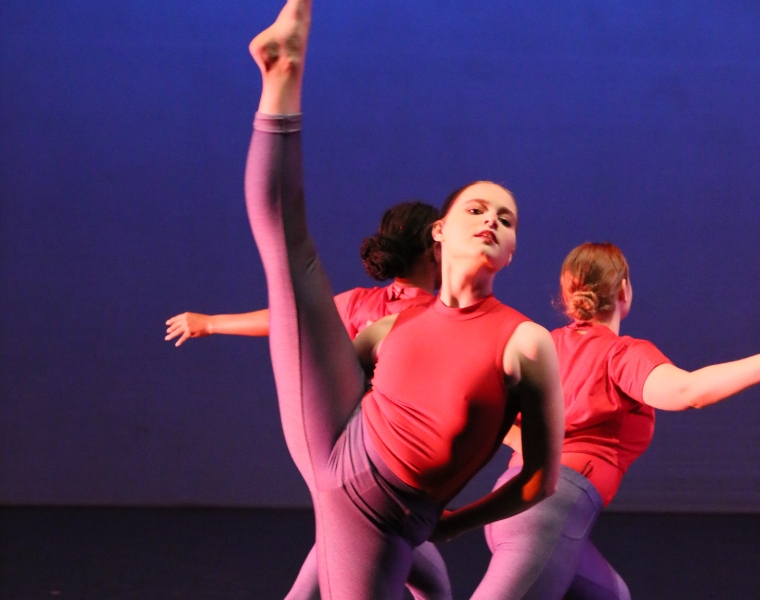 A close up of a dancer kicking her leg with pointed toes with another performer in the background.