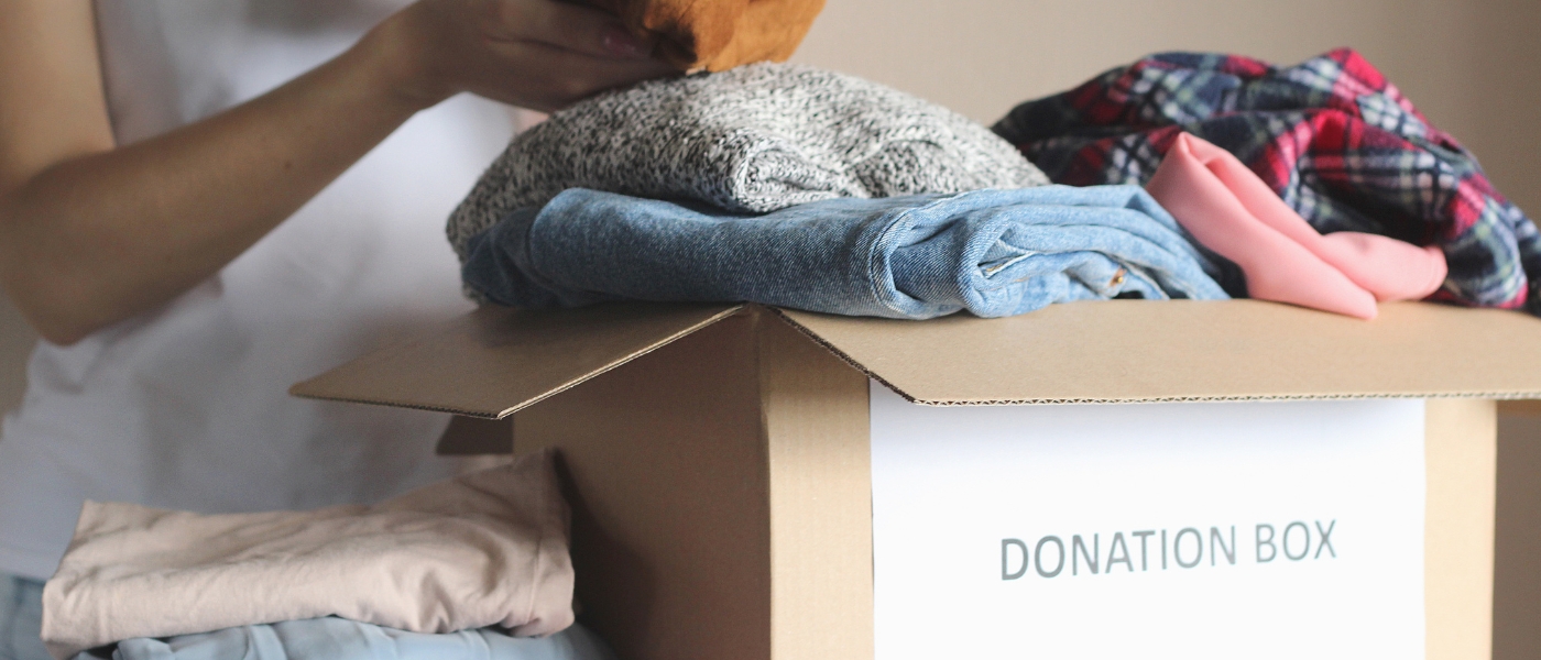 Photo of a person putting clothes in a box that says "donations"