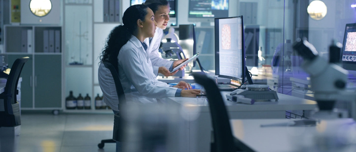 photo of two women in lab coats looking at computer screen