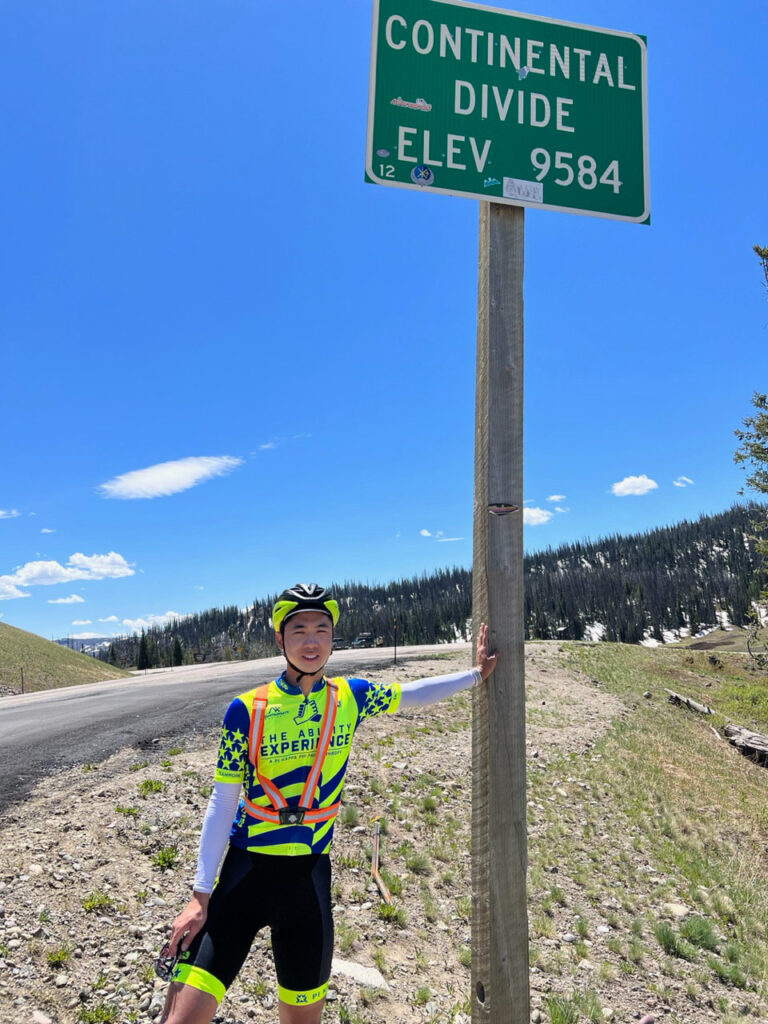 Photo of Steven Wang with a Continental Divide sign that lists the elevation as 9,58