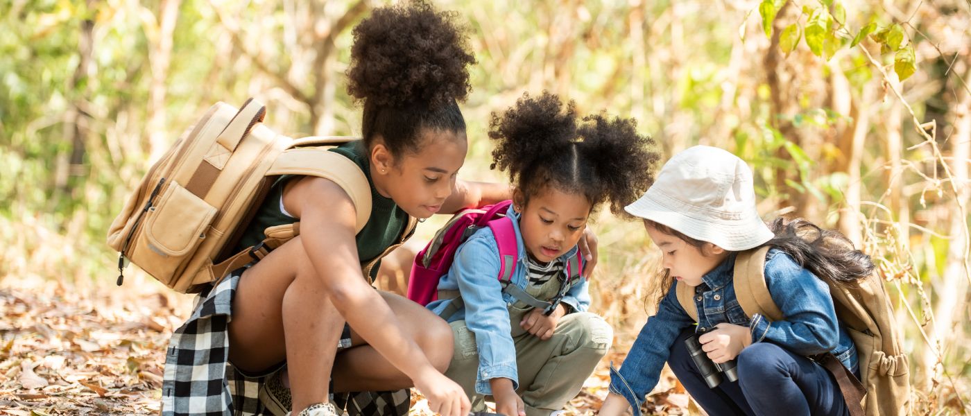 Diverse group of children with backpacks looking at a map in a forest