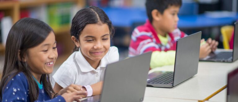A multi-ethnic group of elementary age students are working together on laptops in the computer lab.