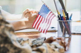 A person in a military outfit sits at a desk with an American flag in a pencil hodler