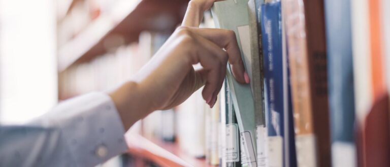 close up of hand reaching for book in a library
