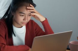 Stressed-looking woman with hand on forehead works on laptop