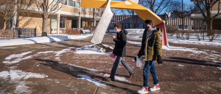 Photo of students walking in front of the Start sculpture in North Residential Village with snow surrounding them