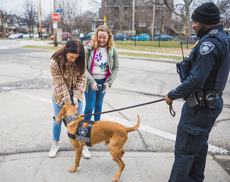 Officer Jimiyu Edwards and K9 Officer Spartie interact with two smiling Case Western Reserve students on a sidewalk