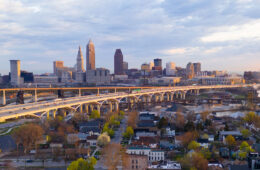 Photo of the Cleveland skyline during sunrise with a highway and a neighborhood in the foreground