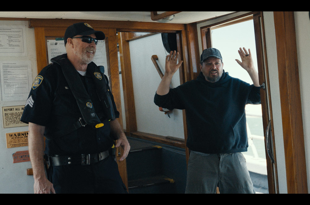 Photo of Kevin Inouye with his hands in the air and an actor portraying a cop next to him in a still image from the Mayor of Kingstown