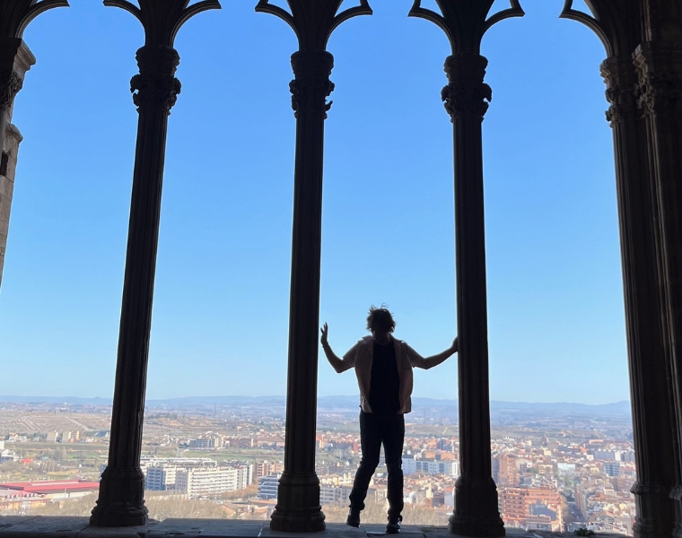 Photo of a student posing between ornate pillars with a city skyscape in the background in Spain