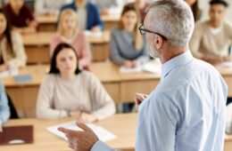 Rear view of mature teacher talking to his student during lecture at university classroom.