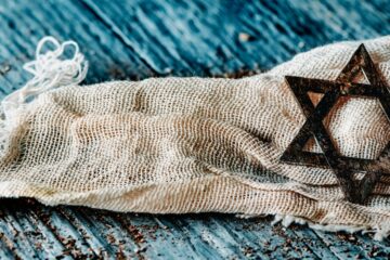 an old pendant in the shape of the star of david, on a ragged piece of cloth, on a gray rustic wooden surface