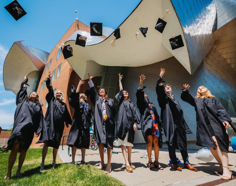 Photo of CWRU graduates throwing their caps in the air in front of the Peter B. Lewis Building. Courtesy of Matt Shiffler