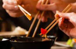 Four sets of chopsticks grabbing Asian food out of various black bowls sitting on a table in a Thai food restaurant. Courtesy of Getty Images