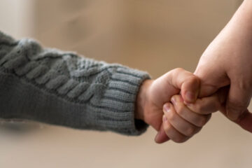 Close up photo of a young child holding the finger of an adult