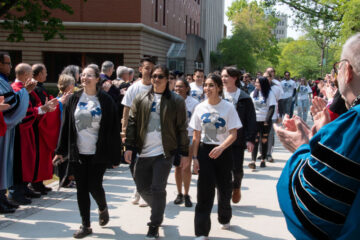 A group of Case Western Reserve University students walk a sidewalk while administrators clap and cheer