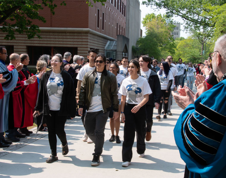 A group of Case Western Reserve University students walk a sidewalk while administrators clap and cheer