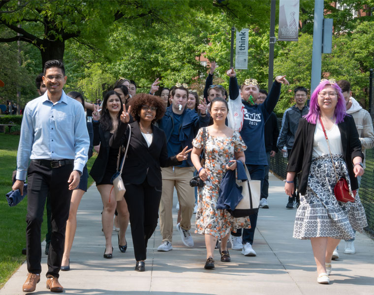 A group of Case Western Reserve University students walk up a sidewalk smiling during commencement clap out