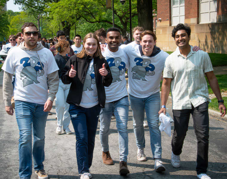 A group of Case Western Reserve University students walk up a sidewalk, with one giving a thumbs up