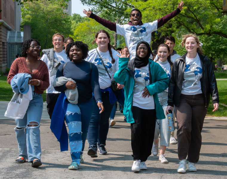 A group of Case Western Reserve University students walk up a sidewalk with one jumping up and holding his hands in the air