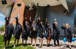 Photo of CWRU graduates throwing their caps in the air in front of the Peter B. Lewis Building