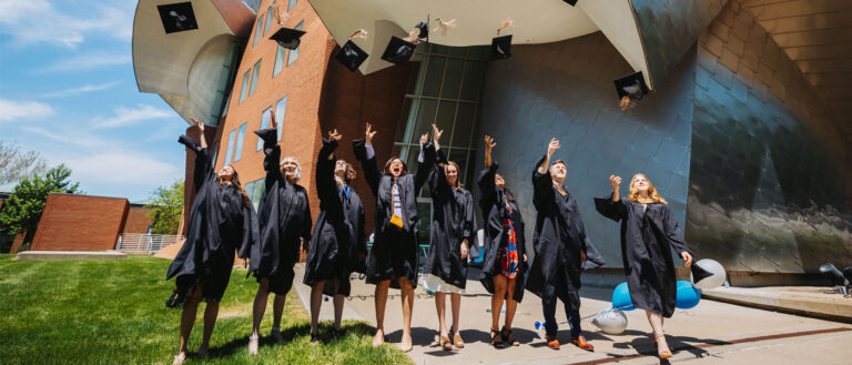 Photo of CWRU graduates throwing their caps in the air in front of the Peter B. Lewis Building