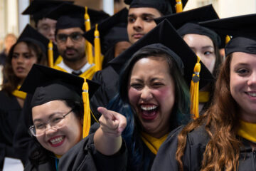 Photo of CWRU graduates celebrating at commencement while one graduate points ahead