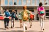 A diverse group of young students with book bags run toward a school building